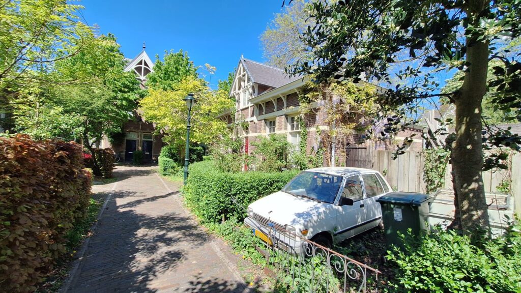 Dit zijn de mooiste hofjes van Den Bosch (ken jij ze allemaal al?) 1 Rustig, oud hofje in Den Bosch met kleine witte huisjes, groen en een geplaveide binnenplaats op een zonnige dag