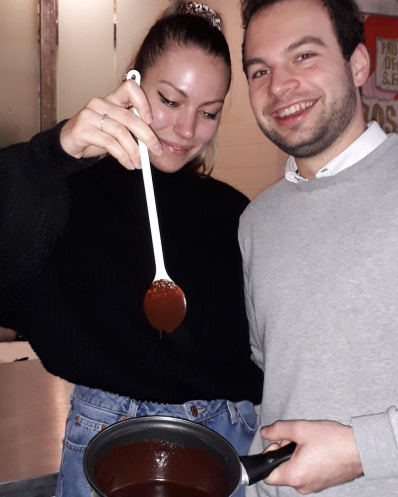 Twee personen bij de Bossche Bollen workshop van Bakkerij Royal in Den Bosch met in de hand een pan gevuld met echte chocolade en een pollepel om te roeren.